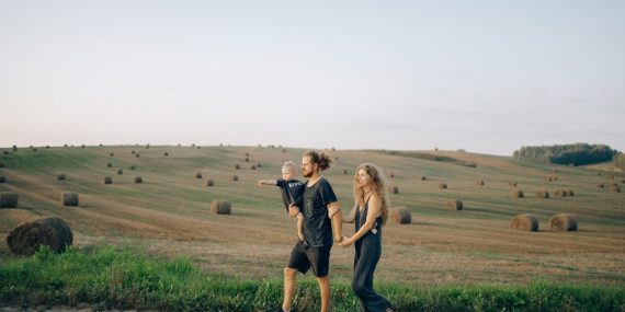 A joyful family walking hand in hand across a picturesque hayfield landscape at sunset.