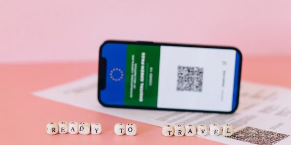 Smartphone displaying digital green pass on a pink surface with travel beads.